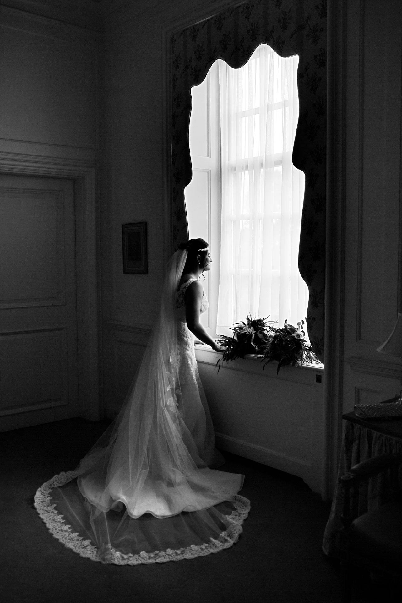 black and white photo of a bride looking out the window of the crane estate at castle hill in Ipswich, MA.