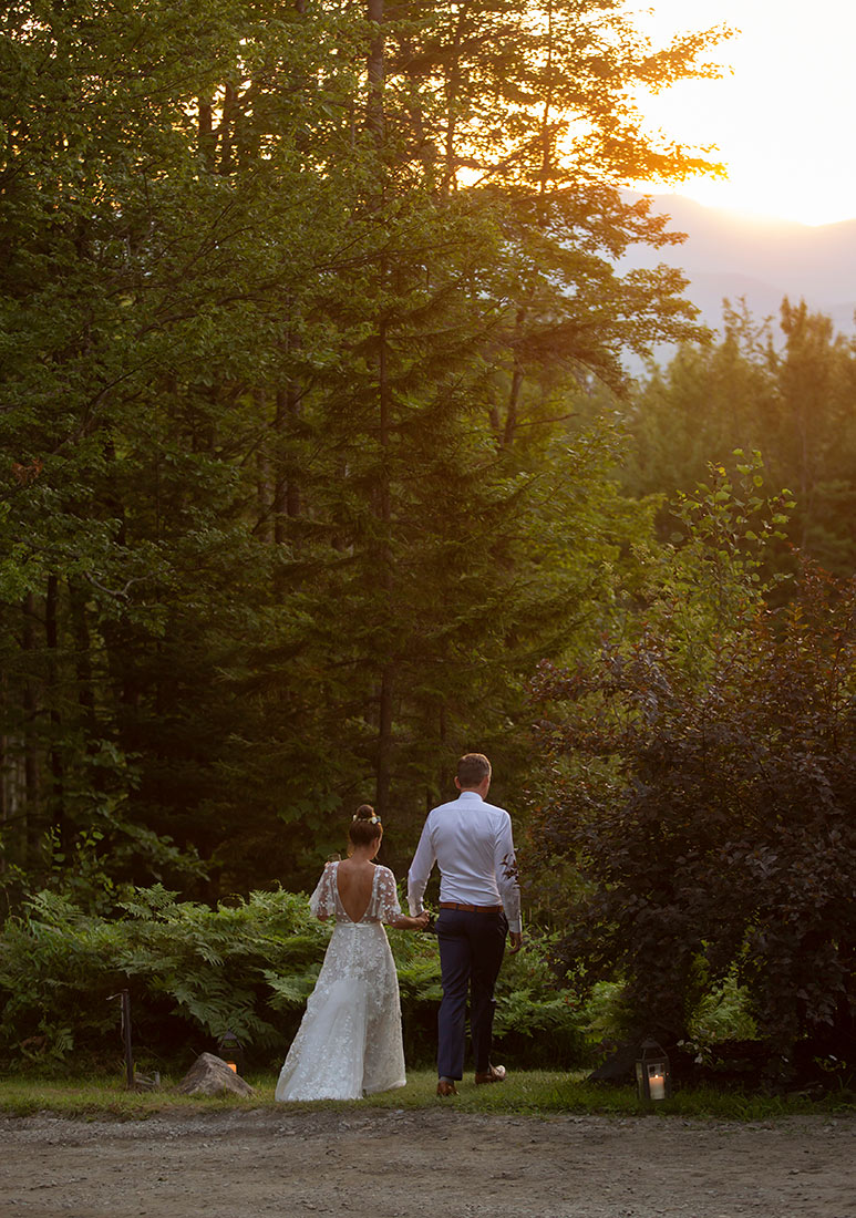 Bride and groom walking through a candlelit garden at dusk. 