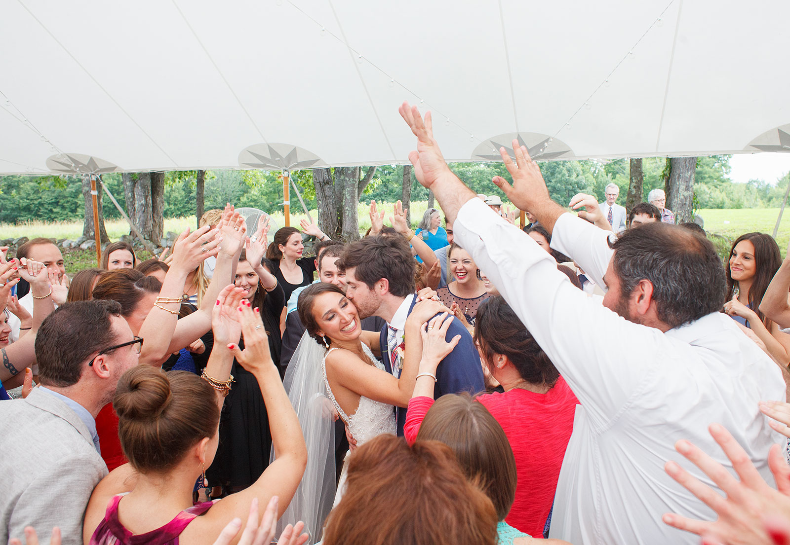 Surrounded by friends and family, a bride and groom embrace on the dance floor of their wedding reception. 